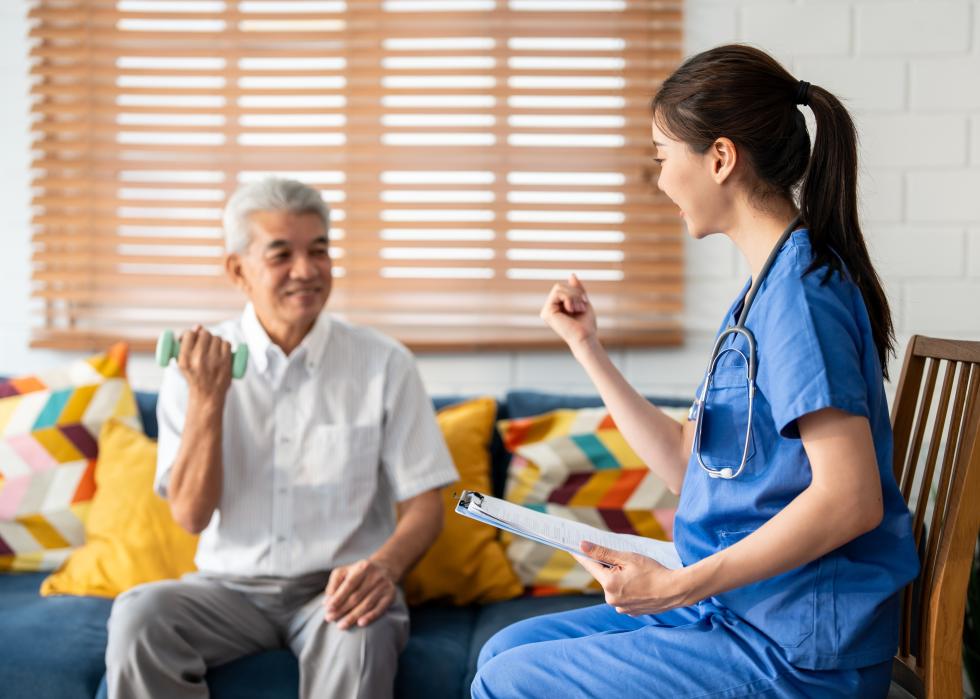 Seated senior man doing physiotherapy with a small hand weight with guidance from a professional.