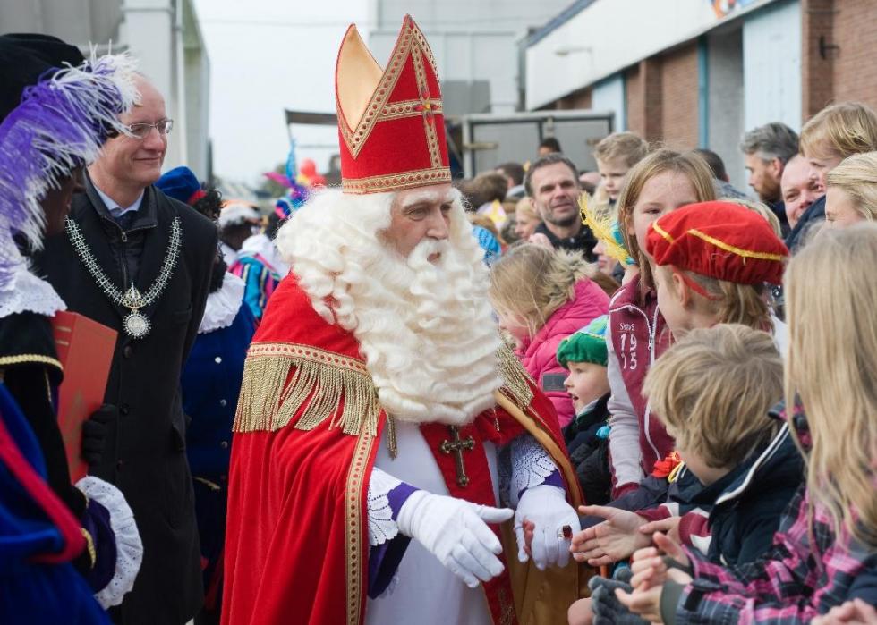 Crowds gather around a man with a long white beard dressed in red, white, and gold.