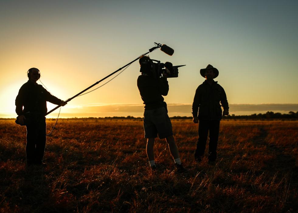 Wide view of the silhouettes of a camerman, sound guy and actor in open field