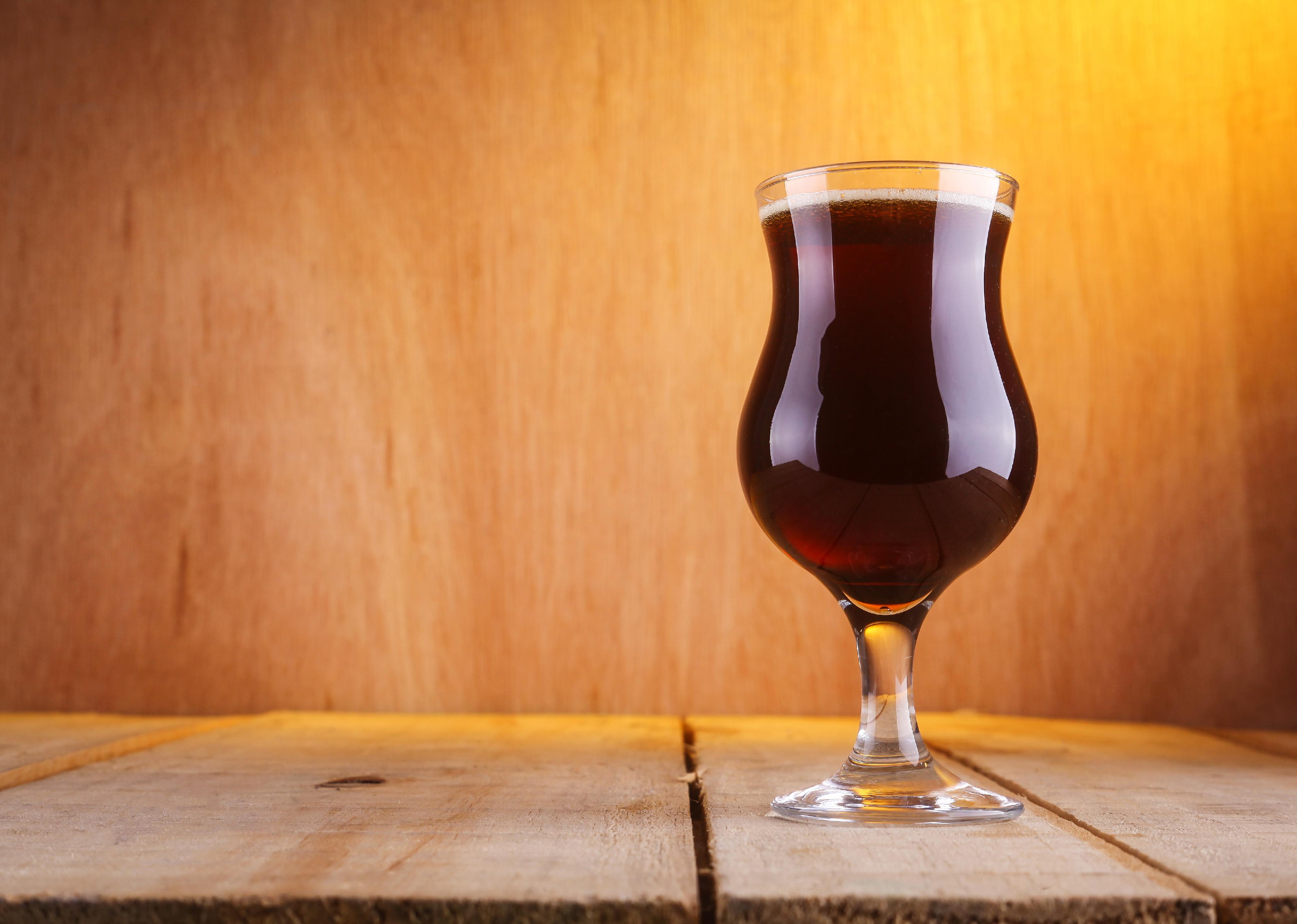 Tulip glass with dark brown beer on a grunge wood surface