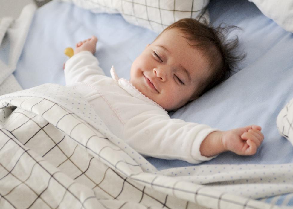 Smiling baby girl lying on a bed sleeping on blue sheets.
