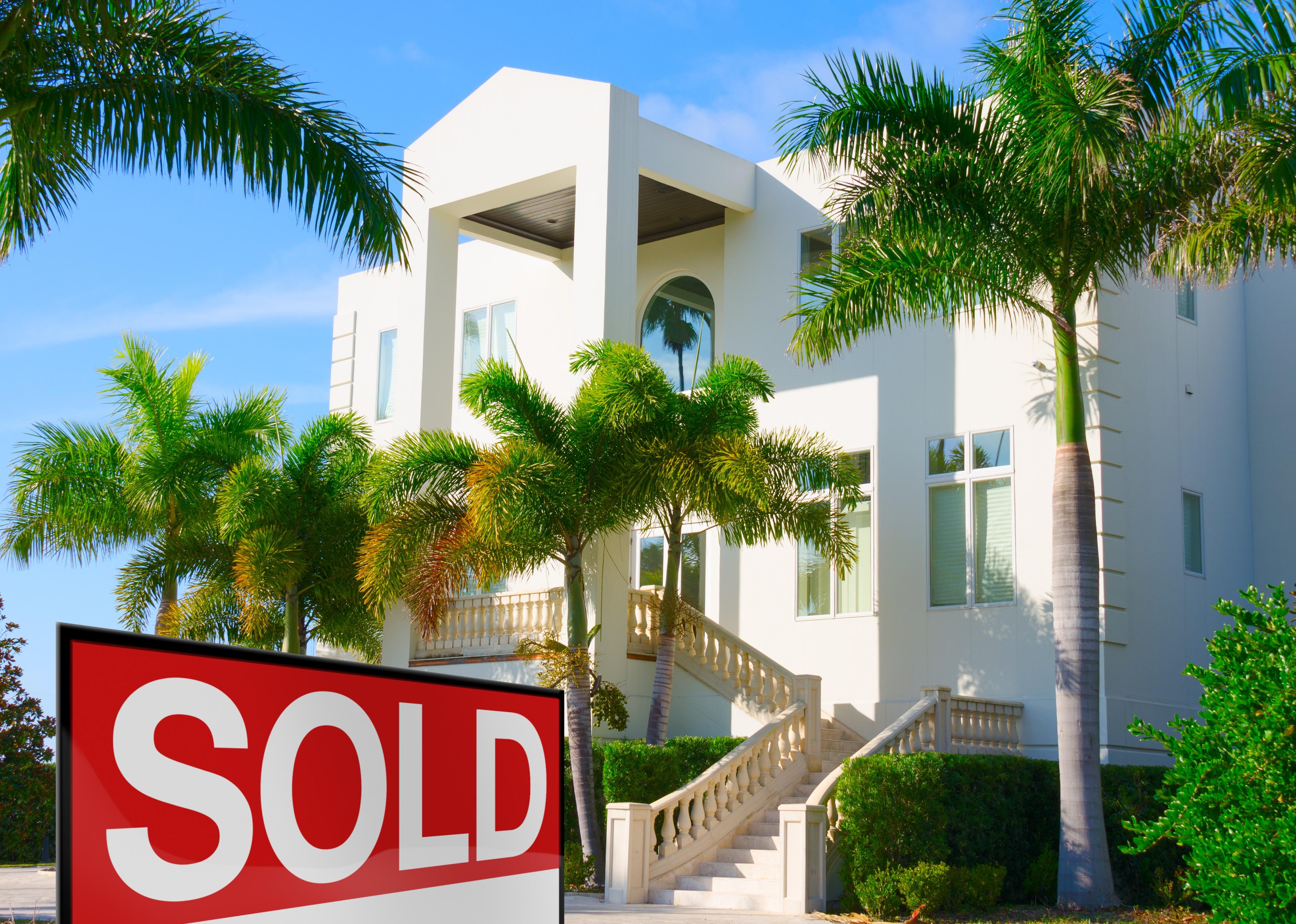 Luxury residential home with stairway and palm trees with a sold sign in the yard.
