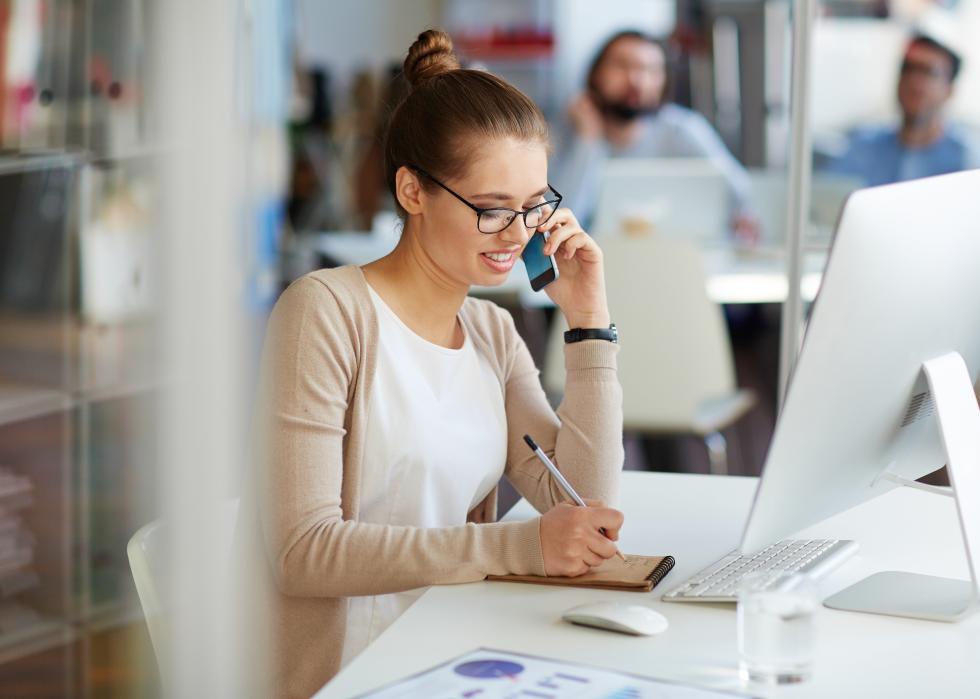 A woman taking notes while on a phone call.