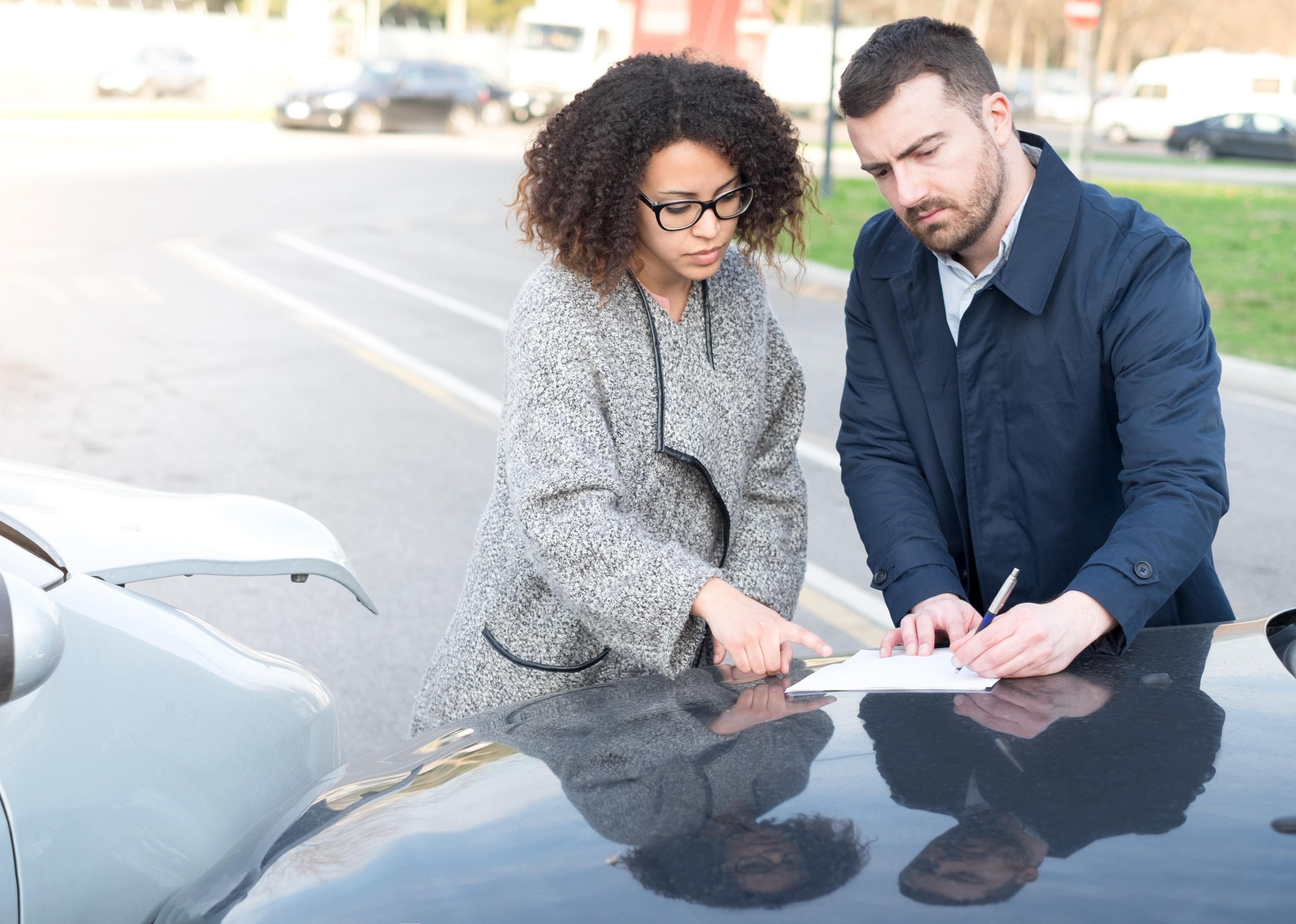 Man and woman filling an insurance car form after car crash.