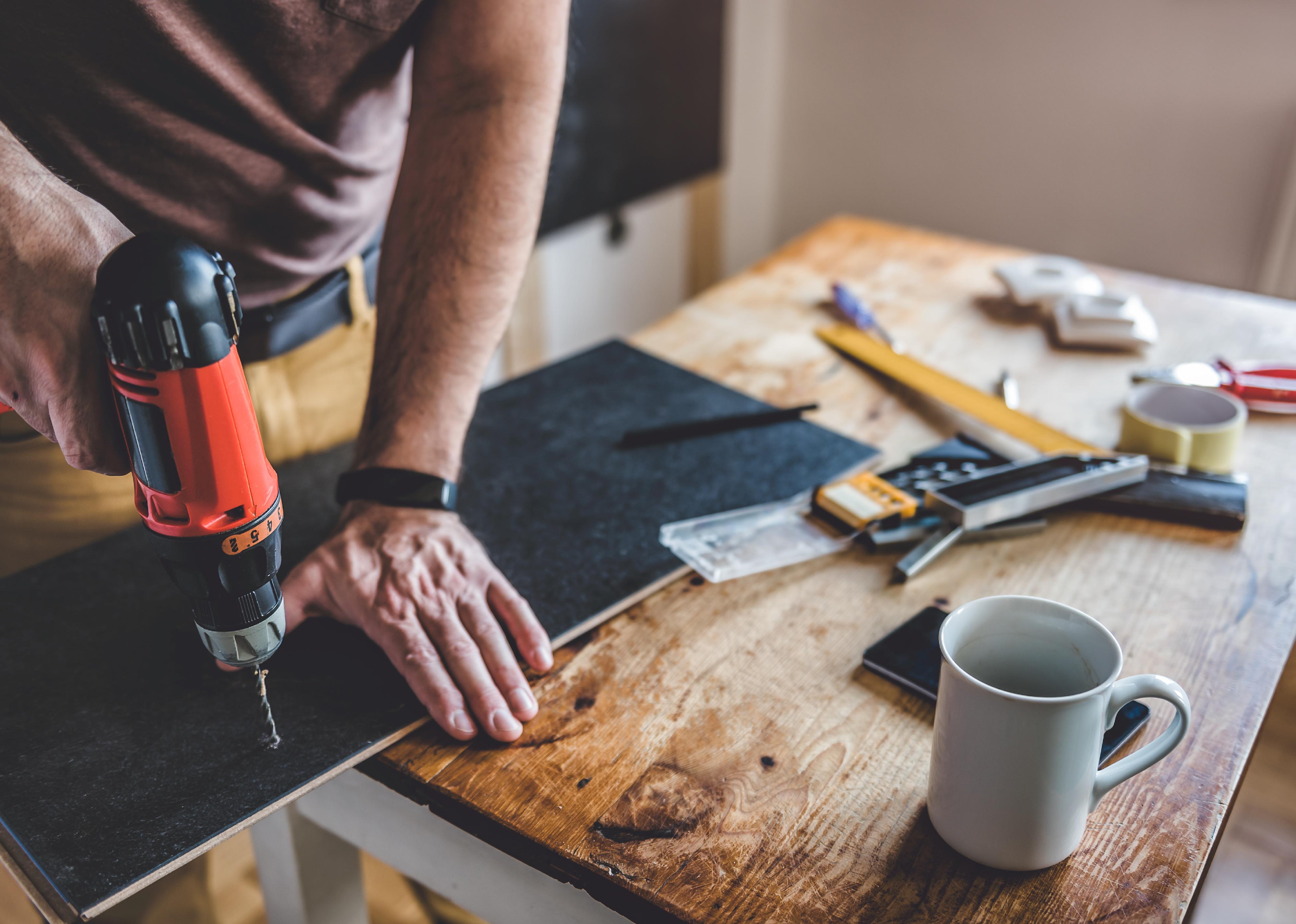 Person drilling laminate with power drill on the table.