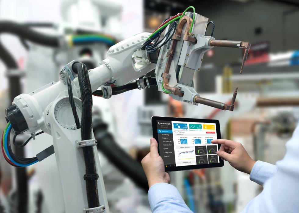 Engineer hand using tablet in front of robot arm machine.