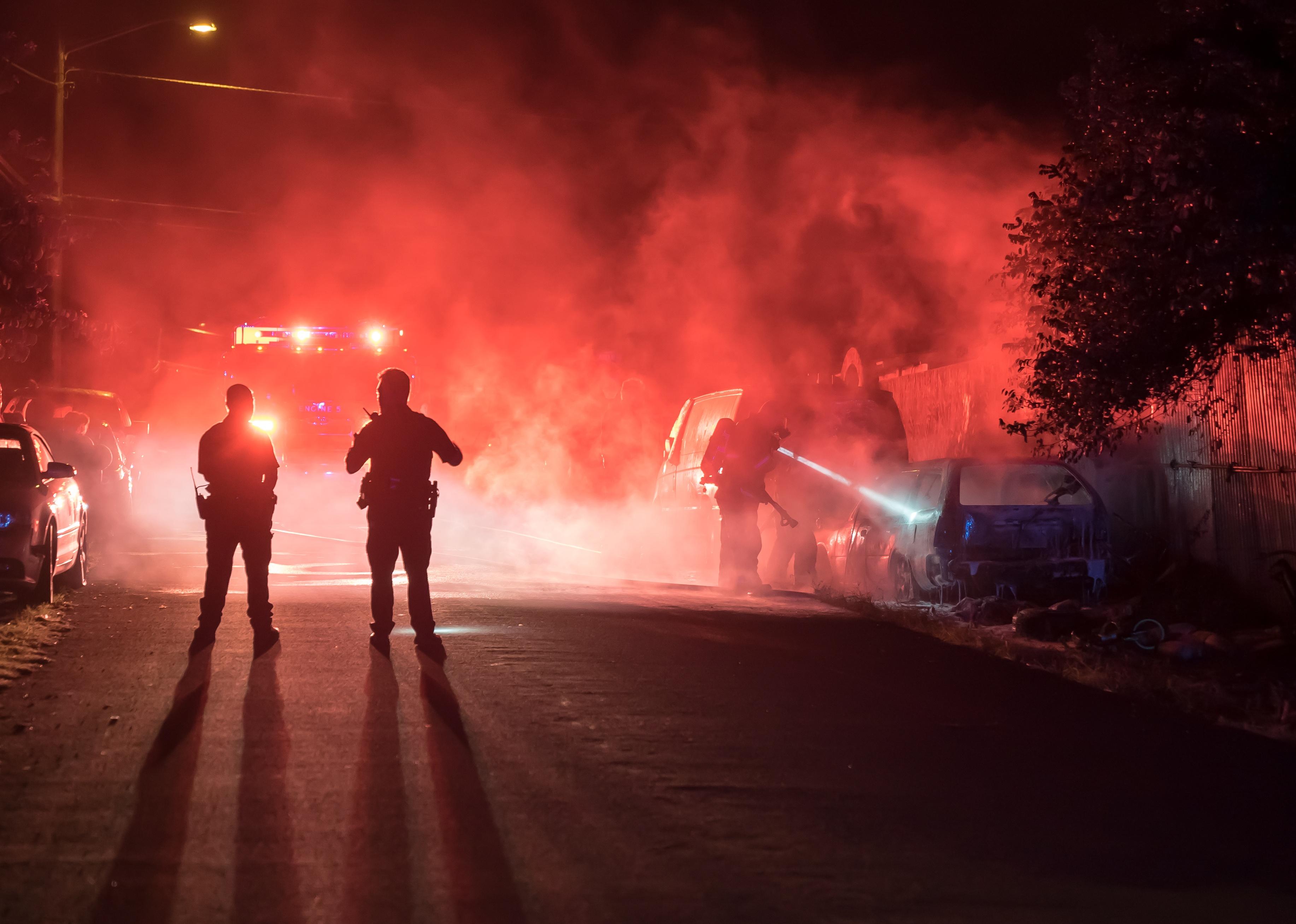 Firefighters and police officers extinguish a vehicle fire in the middle of the night.