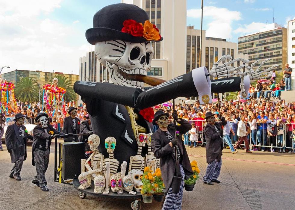 Crowds watch a parade float with a large skeleton and smaller skeletons and skulls below it.