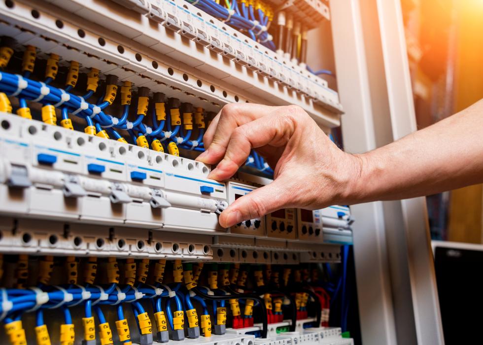 A close up of a hand repairing a switchboard with automatic switches. 