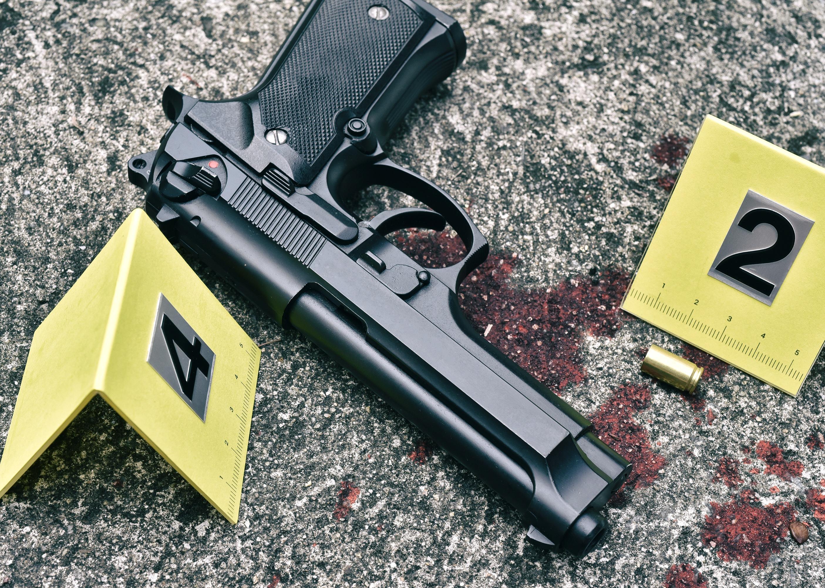 Pistol and bullet shell with blood stain against the crime marker on the ground.