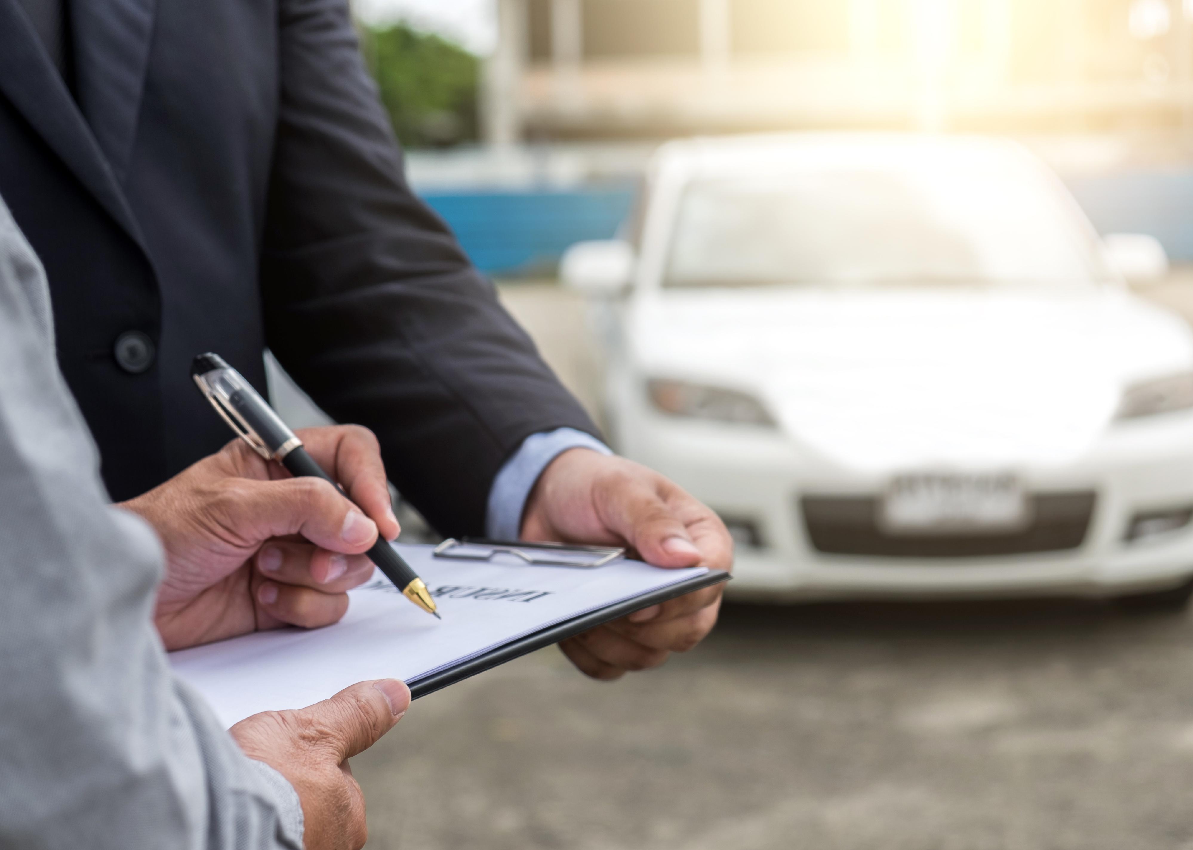 Insurance agent examines car and customer signs claim form