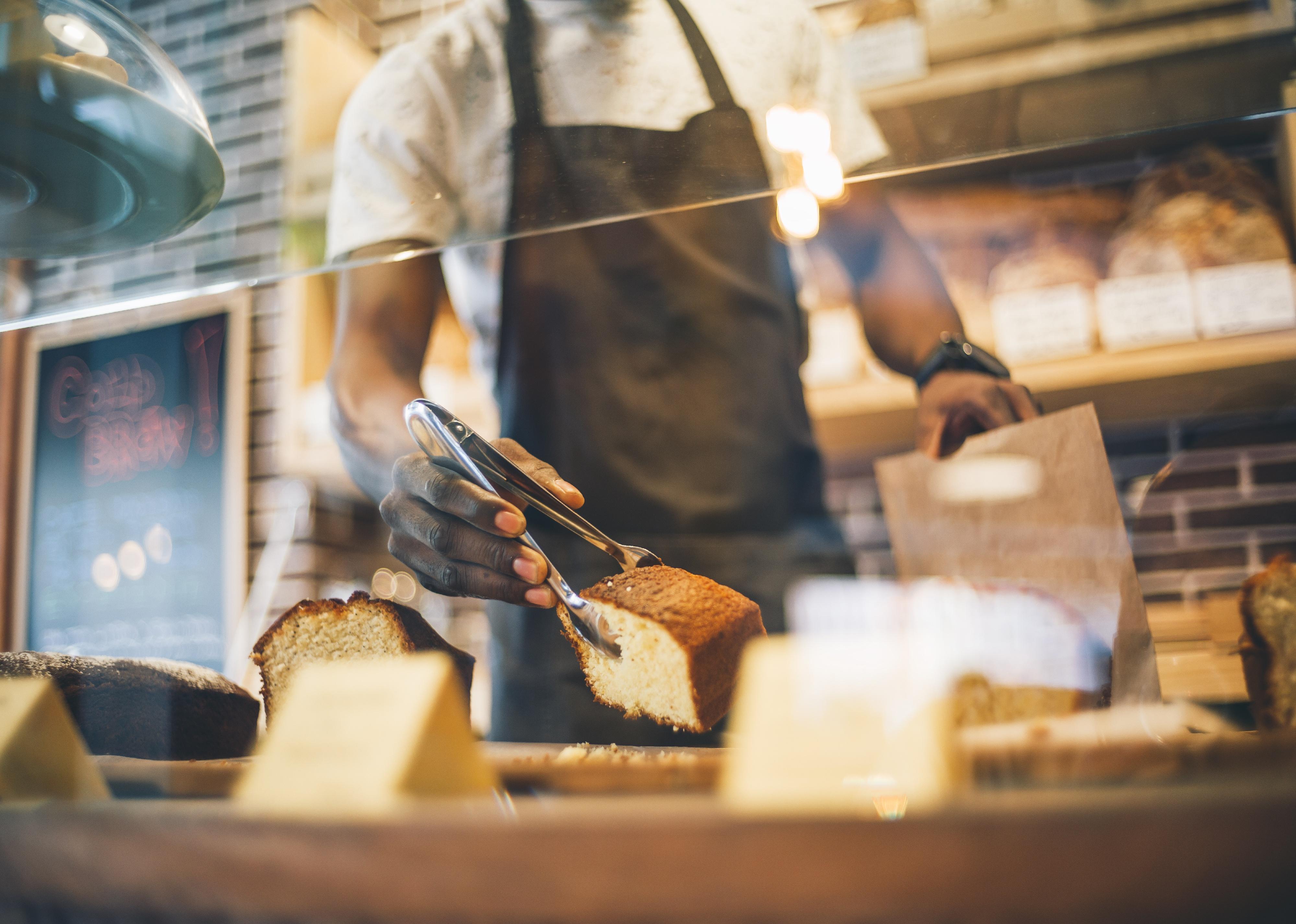 Employee getting something from pastry display in small store.