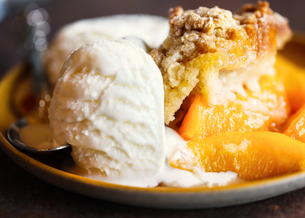 A bowl of peach cobbler with ice cream.