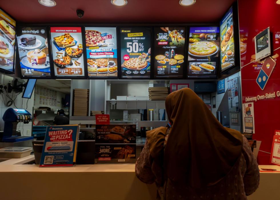 A woman in a hijab waits to order at a Domino's counter.