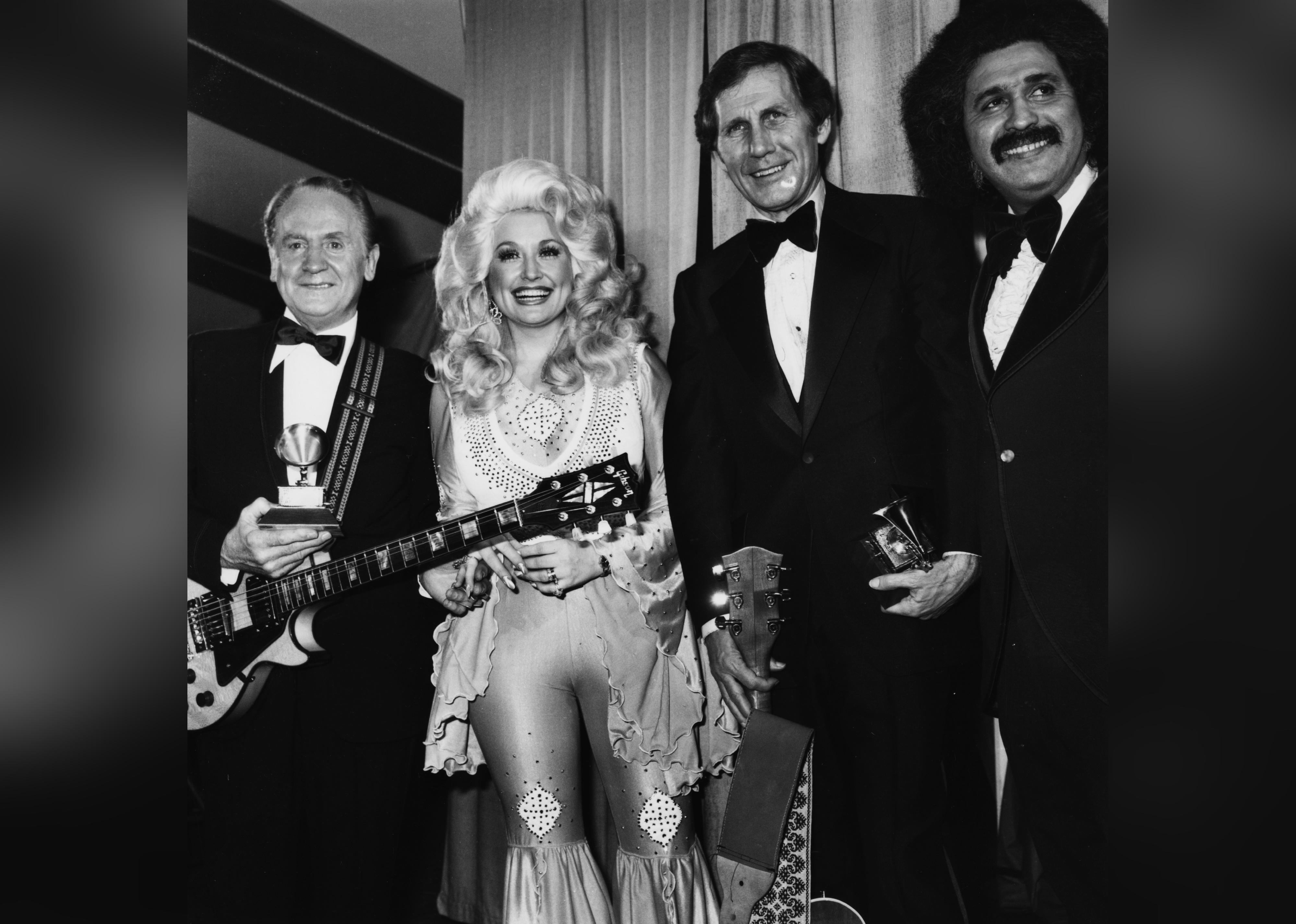 Les Paul, Dolly Parton, Chet Atkins, and Freddie Fender, posing together at the Grammy Awards.