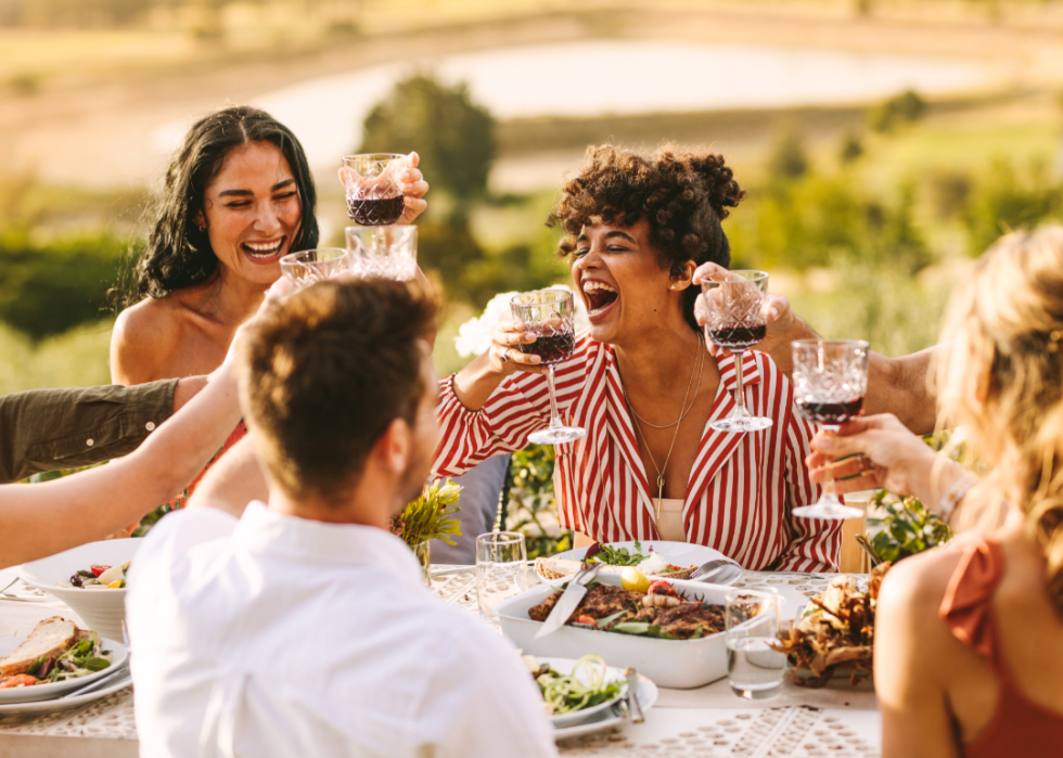 A small group of friends at an outdoor dining table, smiling and cheersing with wine glasses.