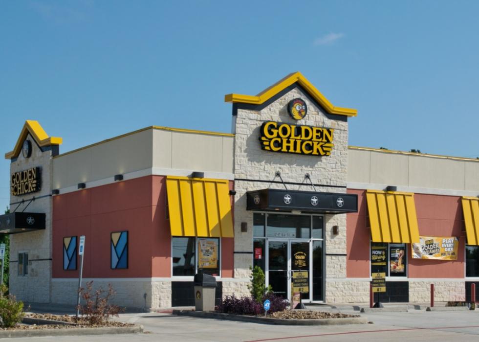 A large corner building with red facade, yellow awnings and yellow sign above the main entrance that says Golden Chick. 