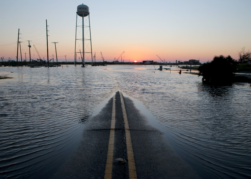 With the sun setting in the distance, only a small sliver of road is seen with the rest of the surrounding area covered in flood water. 