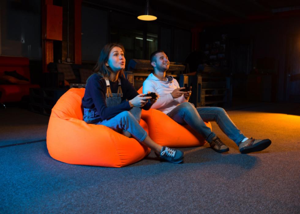 Two young people on orange beanbags playing video games.