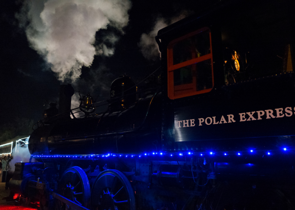 At night, a plume of steam flows out of a steam train with the words The Polar Express on its side.