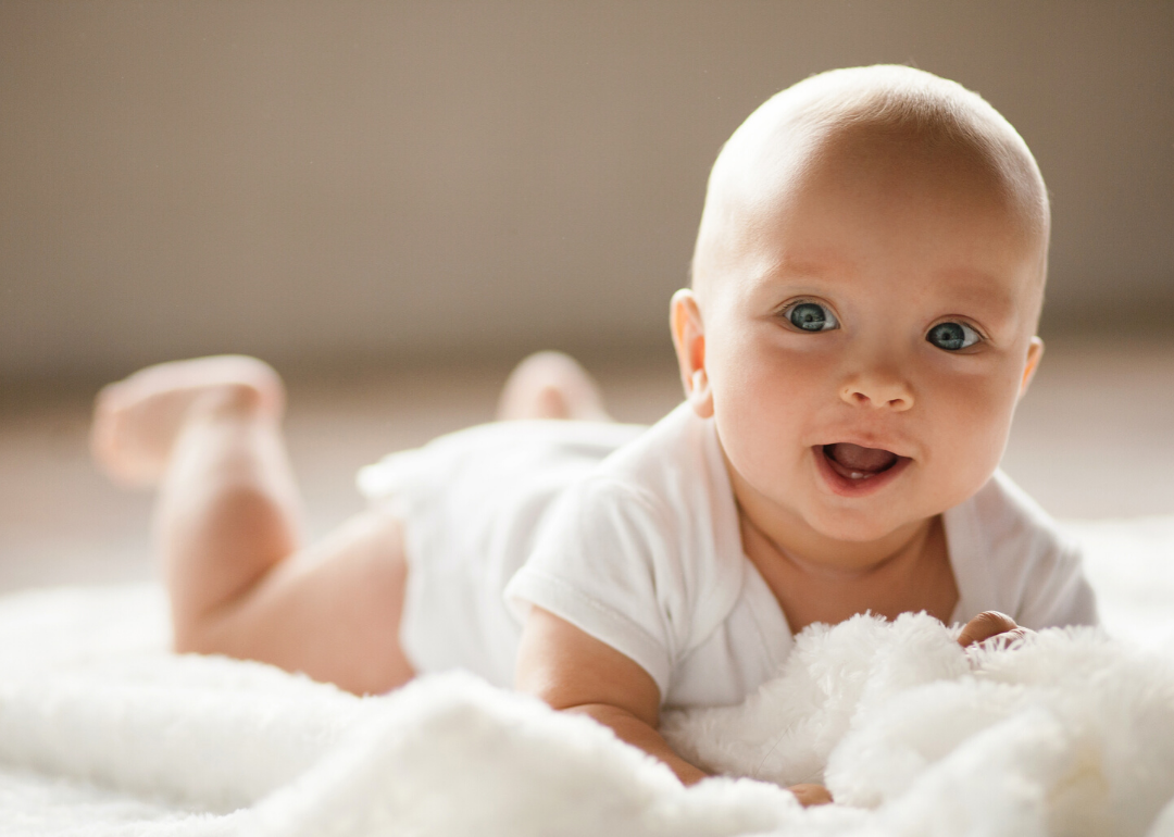 Small baby lying on blanket, smiling and showing two teeth.