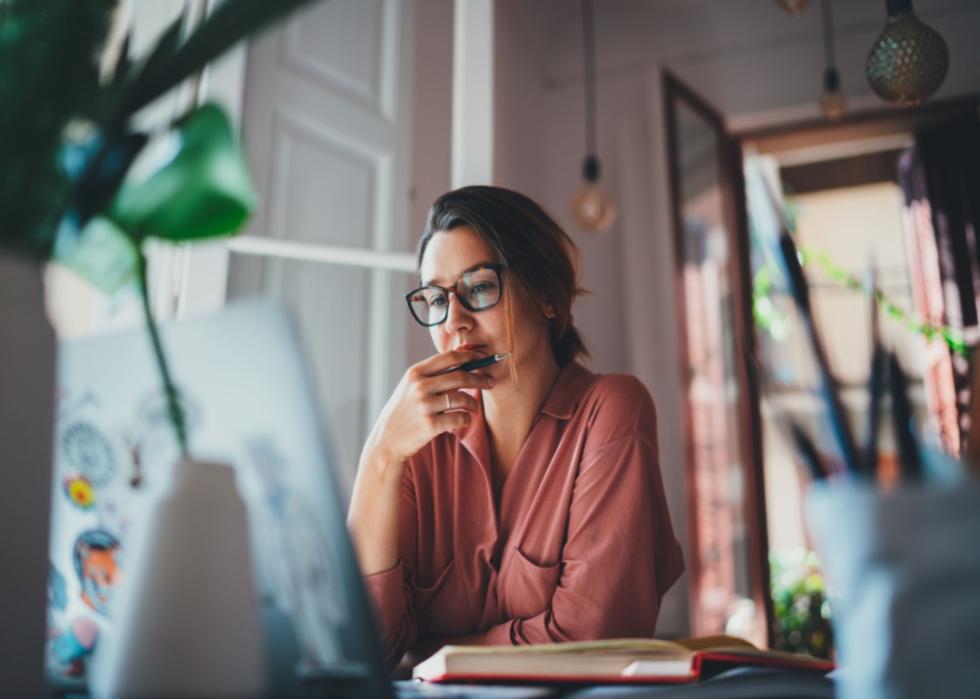 A woman sitting at a desk, looking at a laptop.