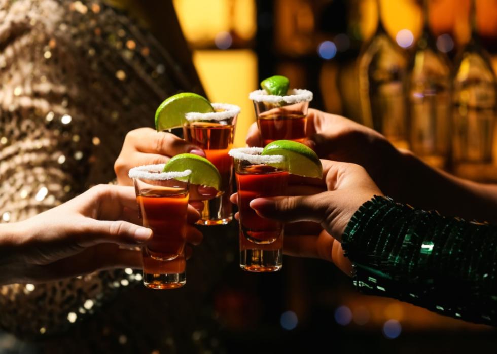 People toasting with tequila shots, which have salt around the rim and a lime wedge.