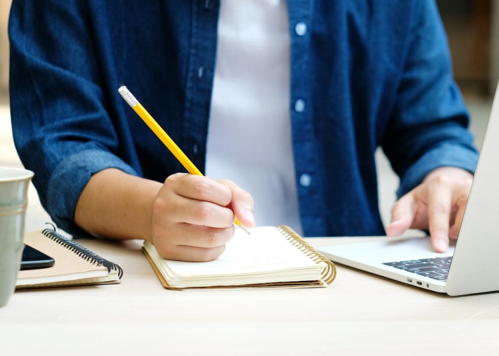 A student writing in a notebook during online class