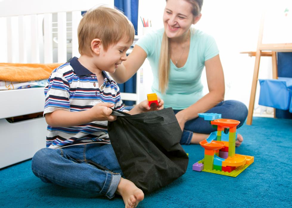 A cute toddler boy tidying up his room and placing toys in a bag