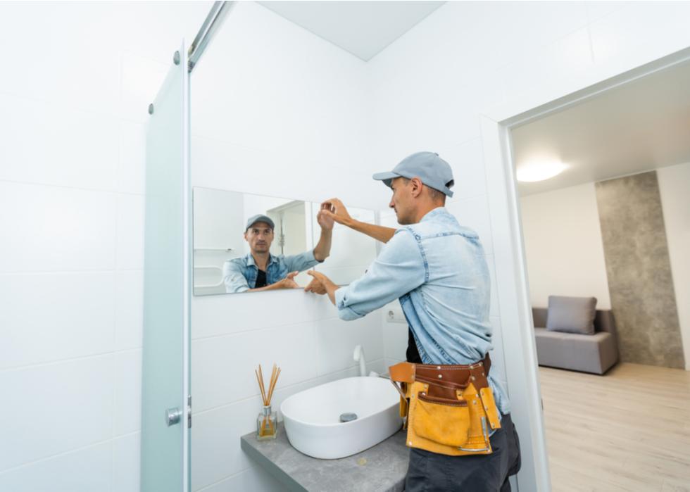 A handyman installing a mirror in a bathroom