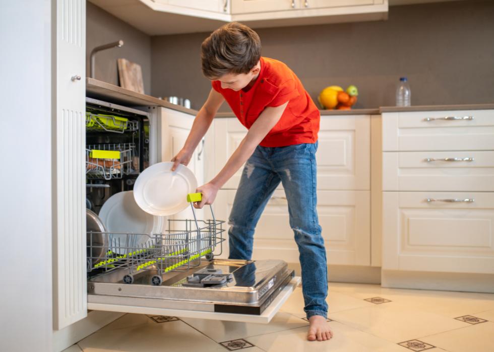 A boy putting dishes into an open dish-washing machine