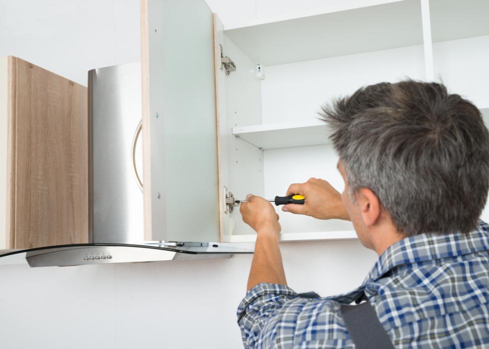 A serviceman installling cabinets with a screwdriver