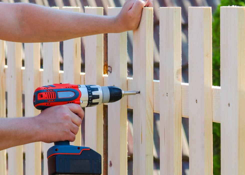 A man building a wooden fence with a drill and screwdriver