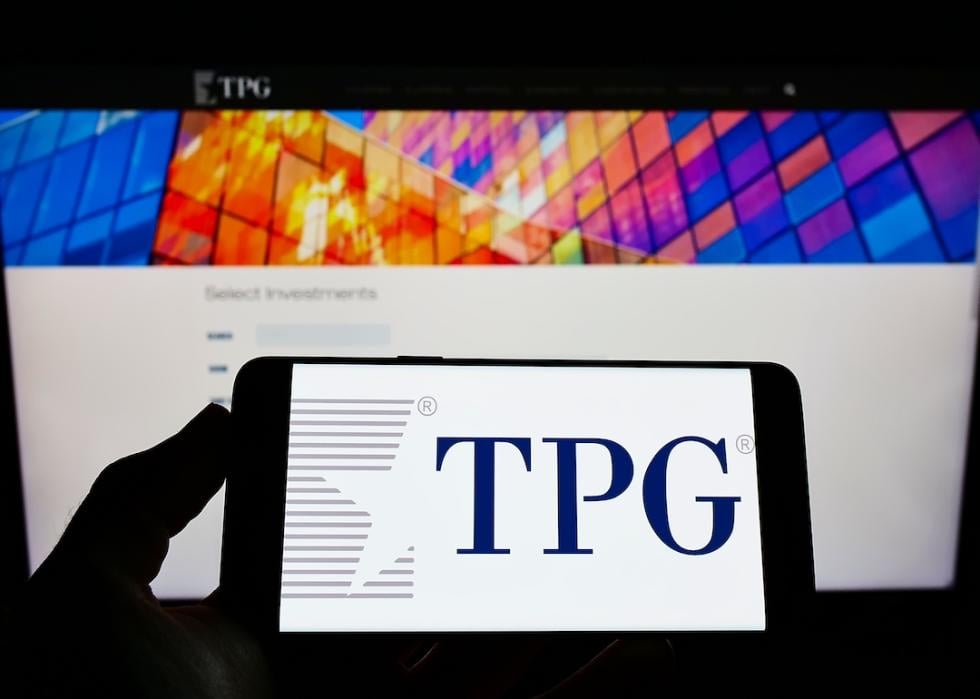 Person holding cellphone with logo of investment company TPG on screen in front of business webpage.