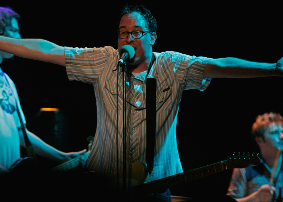 Guitarist sings into a mic with his arms out wide.