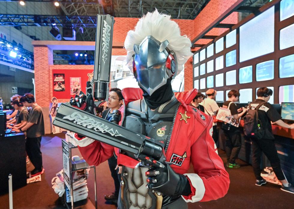 A person posing at a video game show dressed as a character from Zenless Zone Zero surrounded by people playing games.
